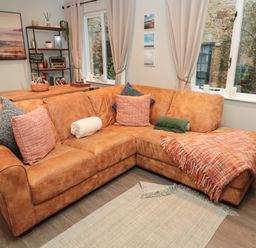 A living room with a brown leather corner sofa and a wooden dining table at Dodds Nook in Alnwick
