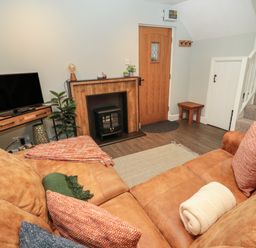 A living room with a brown couch a television a wooden door and carpeted stairs at Dodds Nook in Alnwick