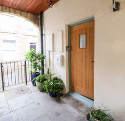 A covered outdoor entrance with a wooden door and several potted plants along the wall at Dodds Nook in Alnwick