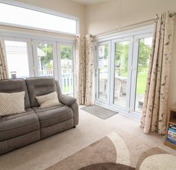 A living room with a sofa pillows board games and glass doors at Waterside Lodge South Lakeland Leisure Village near Carnforth