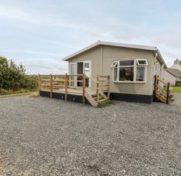 A single-story house with a gravel driveway and wooden porch railings at Porthwen Lodge in Bull Bay near Cemaes Bay