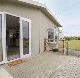 A wooden deck outside a house with open glass doors showing a kitchen with stools at Porthwen Lodge in Bull Bay near Cemaes Bay