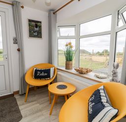 A small sitting area with two yellow chairs and a round table near windows with curtains at Porthwen Lodge in Bull Bay near Cemaes Bay
