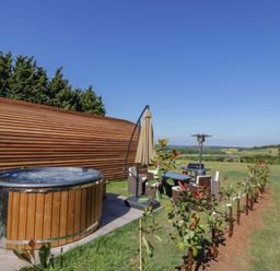 An outdoor area with a wooden hot tub a table with chairs an umbrella and young plants in a garden at Tamina in Hillhampton Great Witley