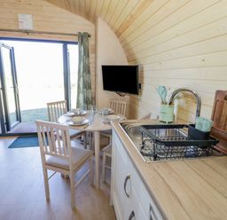 A kitchen and dining area with a round table set for four near open glass doors at Tamina in Hillhampton Great Witley