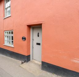 An exterior view of a building with an orange wall a gray door a window and a street sign at Forge House in Cley Next The Sea