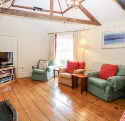 A sitting room with armchairs cushions wooden floor and exposed beams at Forge House in Cley Next The Sea