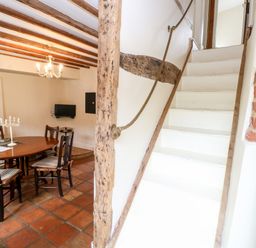 A dining area with wooden table and chairs next to white stairs with rope handrail at Forge House in Cley Next The Sea