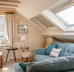 A living room with blue sofas a window seat with cushions two small tables a lamp and skylights at Goody in Hope Cove