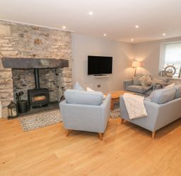 A living room with light blue sofas a wooden floor and a stone fireplace at Fishermans Cottage in Malltraeth