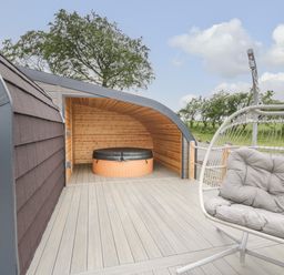 An outdoor deck area with a covered hot tub and a cushioned hanging chair at Laird Lodge 5 Lochmaben