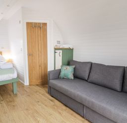 A room with a gray sofa wooden floor a bed with white bedding and a wooden door at Laird Lodge 5 in Lochmaben