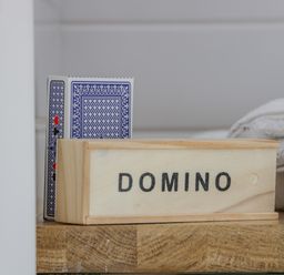 A box labeled domino next to a deck of playing cards and folded towels on a wooden surface at Laird Lodge 5 in Lochmaben