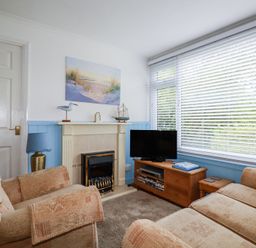 A living room with armchairs a fireplace a television on a wooden stand and a large window with blinds at 8 The Park in Kilkhampton