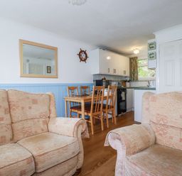 A sitting area with two beige sofas and a dining area with a wooden table and four chairs next to a kitchen at 8 The Park in Kilkhampton