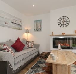 A living room with a grey sofa with cushions a wooden coffee table a wall clock and an electric fireplace at The Hideaway in Lympsham near Brean