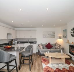 An open plan kitchen and living area with grey chairs, a grey sofa, a wooden coffee table, and a fireplace at The Hideaway in Lympsham near Brean