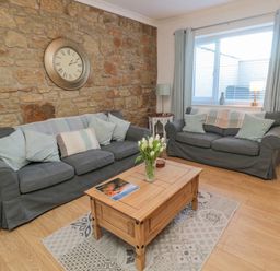 A sitting room with two grey sofas a wooden coffee table and a stone wall with a clock at Redshank in Amble