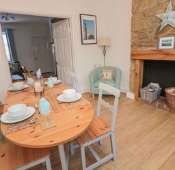 A dining room with a wooden table set for four next to a stone fireplace with baskets and a blue armchair at Redshank in Amble