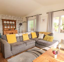 A living room with a grey sofa with yellow cushions a wooden cabinet displaying plates and a wooden coffee table with flowers at Dragonfly Lodge in Worthen near Minsterley