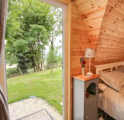 A bedroom with a bed next to a nightstand and an open door leading to a grassy outdoor area at The Pod in Worthen near Minsterley