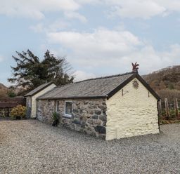 A stone cottage with a gravel driveway and plants near hills at Tyn Y Cefn Near Blaenau Ffestiniog