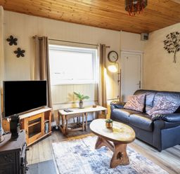 A living room with a black leather sofa two patterned cushions a wooden coffee table and a television on a wooden stand at Tyn Y Cefn Near Blaenau Ffestiniog