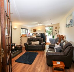 A living room with two leather sofas a small black rug a wood burning stove and a kitchen area at The Retreat in Pedairffordd near Llanrhaeadr-Ym-Mochnant