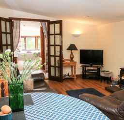A living room with a table and flowers a television and a wood stove at The Retreat in Pedairffordd near Llanrhaeadr-Ym-Mochnant