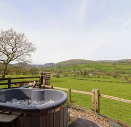 An outdoor hot tub with a wooden fence overlooking green fields and hills at The Retreat in Pedairffordd near Llanrhaeadr-Ym-Mochnant
