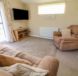 A living room with a brown sofa and armchair a wall-mounted TV and a wooden TV stand with decorations at Number 15 in Carnforth
