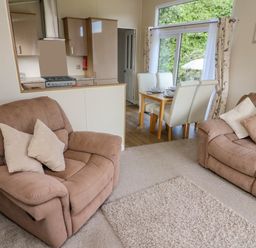 A living room with two beige recliner sofas and cushions overlooking a dining area with four white chairs and a wooden table next to a window at Number 15 in Carnforth