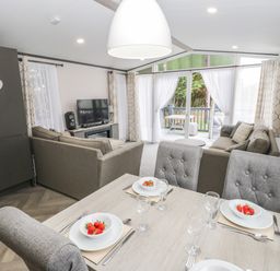 A dining area with a table set with plates of strawberries and glassware next to a living room with sofas and a TV at Finch 59 in Cayton