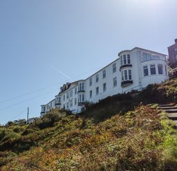 White multi-story buildings on a hillside with a concrete stairway and vegetation at Starfish in Sennen Cove
