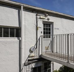 An exterior view of a white building with a metal balcony and doors labeled flats at Starfish in Sennen Cove