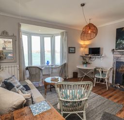 A living room with wicker chairs a wooden coffee table a sofa and a fireplace at Starfish in Sennen Cove
