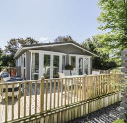 A wooden deck with chairs and a table outside a building surrounded by trees at Orchard Lodge in Llanengan near Abersoch