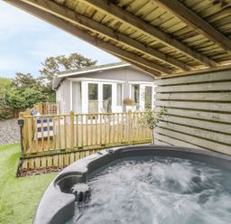 A covered hot tub next to a wooden deck with outdoor furniture and a house in the background at Orchard Lodge Llanengan near Abersoch