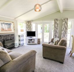 A living room with two sofas a fireplace a television on a stand and glass doors at Orchard Lodge in Llanengan near Abersoch