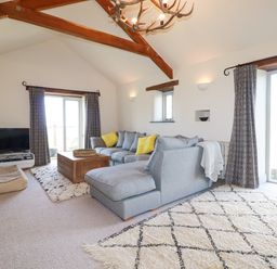 A living room with a gray sectional sofa with yellow pillows wooden coffee table and a television on a stand at Penpethy Farm in Tintagel