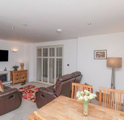 A living room with leather recliner chairs a wall-mounted TV and a wooden dining table with flowers at Above & Beyond Whitby