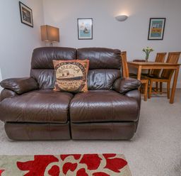 A brown leather sofa with a decorative pillow in front of a dining table with chairs and wall art at Above & Beyond Whitby