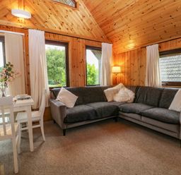 A corner living room with grey sofas and white dining table with chairs at Lodge 16 in Lanteglos near Camelford