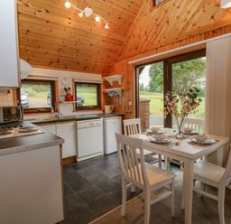 A kitchen and dining area with a white table set for four and a view of the outside at Lodge 16 in Lanteglos near Camelford