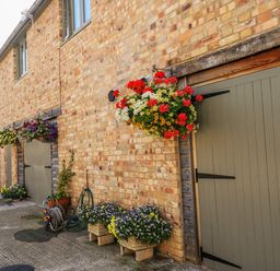 A brick building exterior with hanging flower baskets and large green doors at The Mews in Bovey Tracey near Chudleigh Knighton