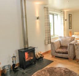 A living room with a wood burning stove armchairs and a dining table at The Mews in Bovey Tracey near Chudleigh Knighton