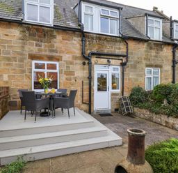 An outdoor patio area with a table and four chairs next to a stone house at Maypole Cottage in Fylingthorpe