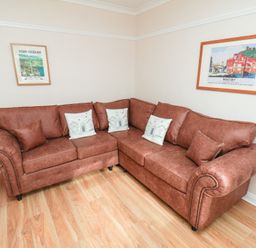 A living room with a corner sofa and framed pictures at Maypole Cottage in Fylingthorpe