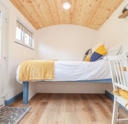 A small bedroom with a bed a white chair a desk and a wooden ceiling at Sunflower Sparnon Gate near Illogan