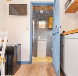 A small kitchen area with a white chair and mini fridge a blue door leading to a bathroom at Sunflower Sparnon Gate near Illogan